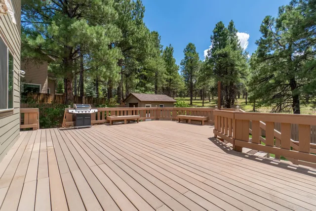 Spacious wooden deck with railing, hot tub, and pine trees under a clear blue sky
