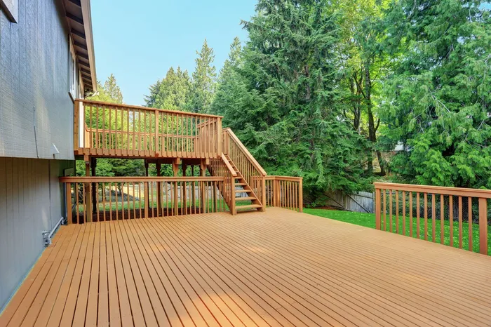 Wooden backyard deck with railing and stairs beside a house, surrounded by green trees