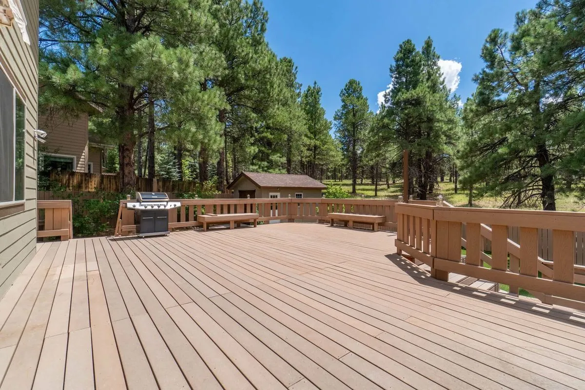 Spacious wooden deck overlooking pine trees and a small cabin under a clear blue sky