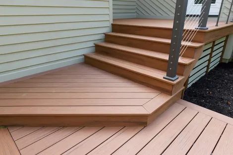 Wooden deck with steps and railing beside a house, showing tan and brown composite boards.