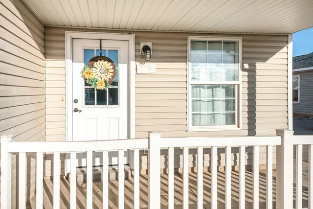 Front porch with white railing, beige siding, white door with wreath, and a window beside it
