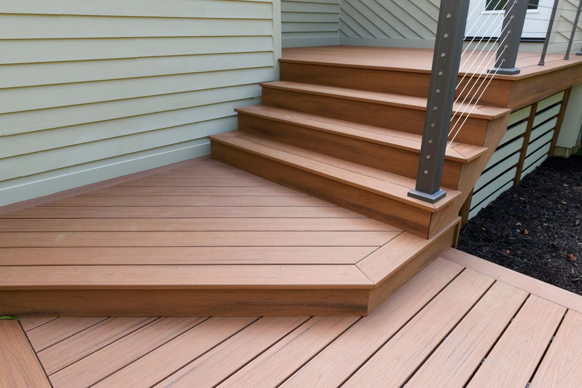 Wooden deck stairs with brown steps and light siding, leading to a raised outdoor deck.