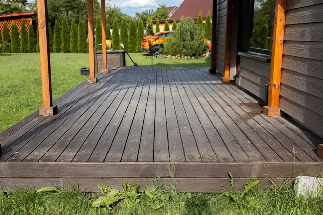 Weathered wooden porch with orange posts overlooking a green yard and houses in the distance