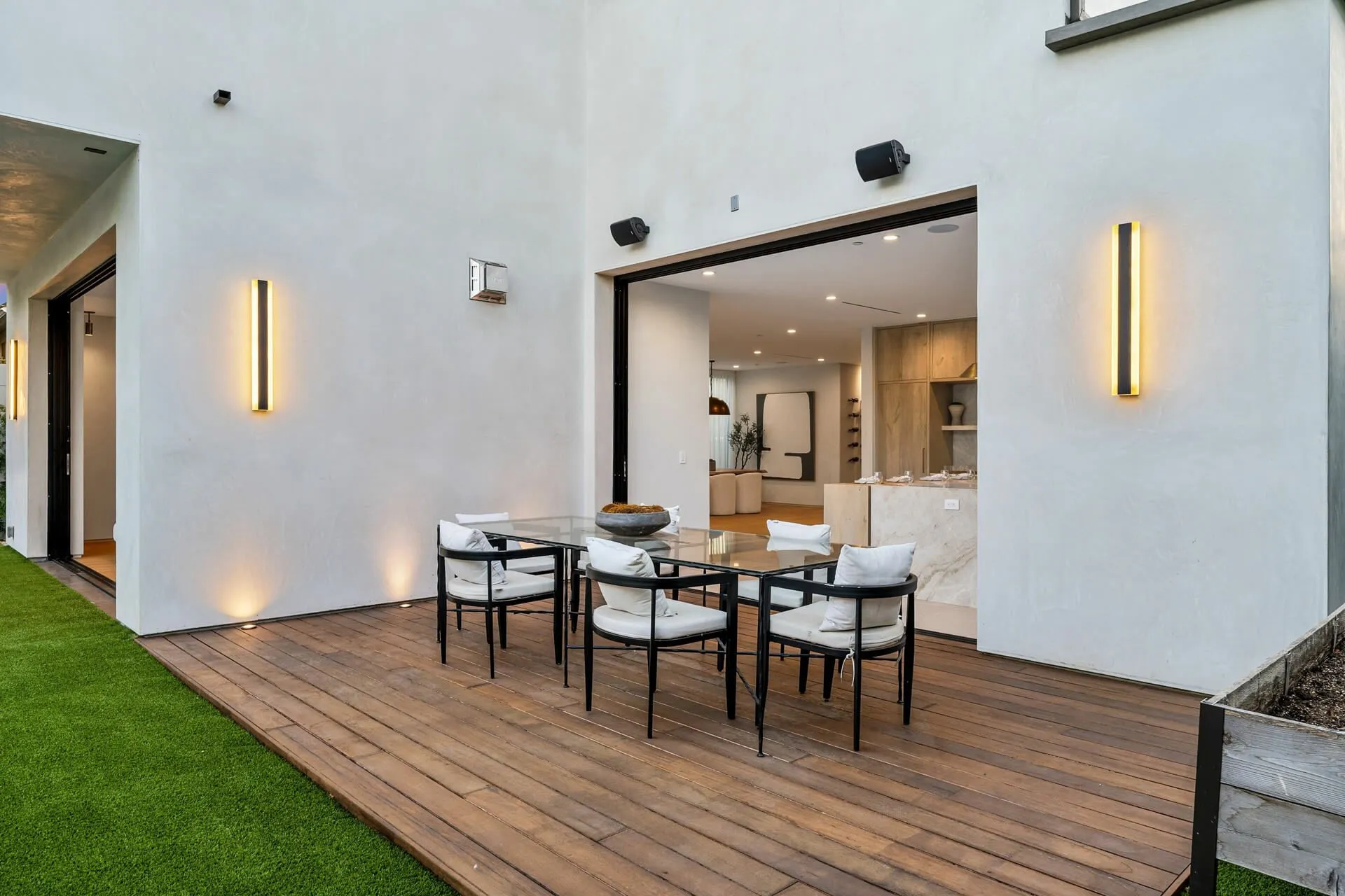 Modern patio with outdoor dining table and chairs beside a white house wall and open sliding doors